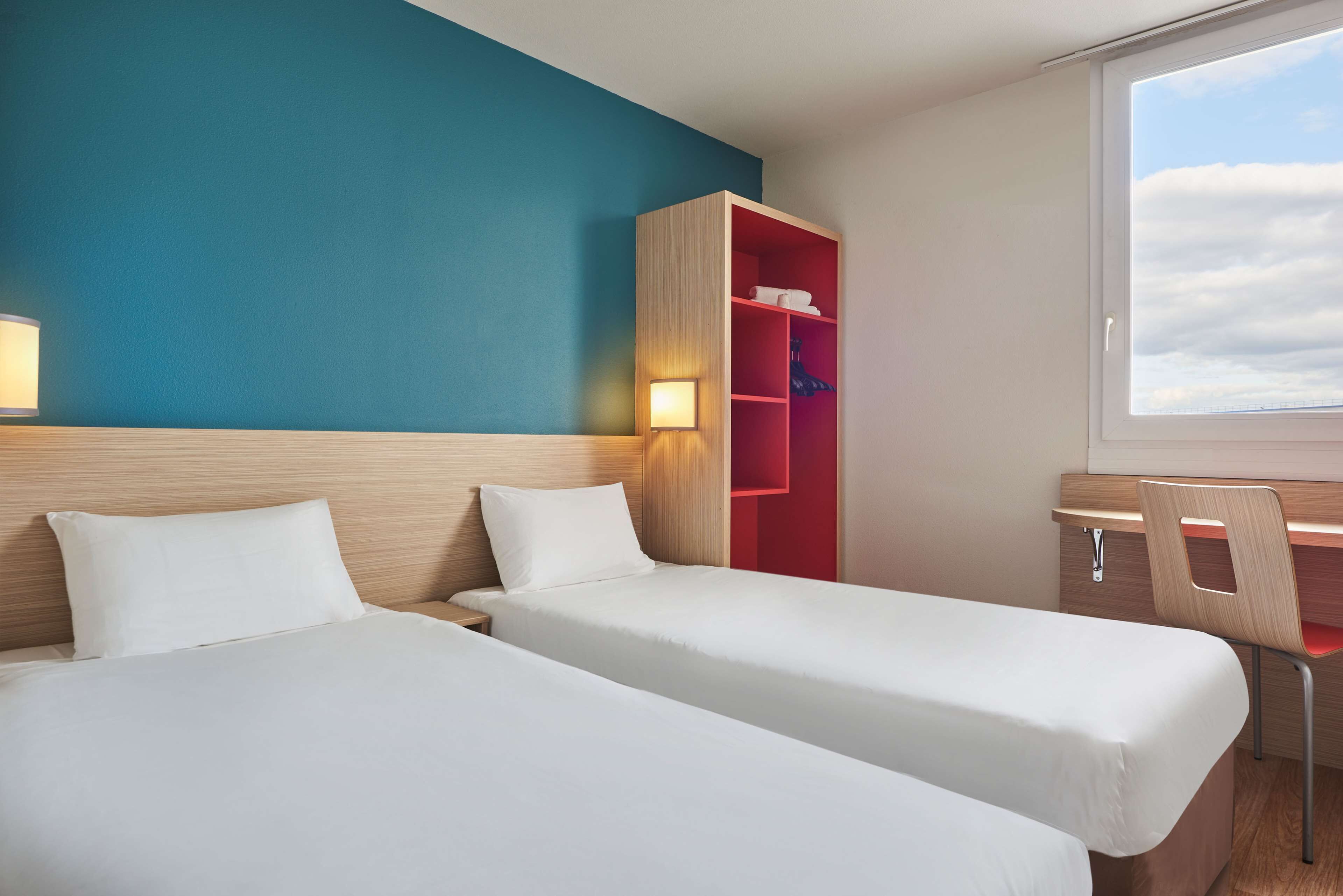 A hotel room with two beds, a desk, and a wardrobe.