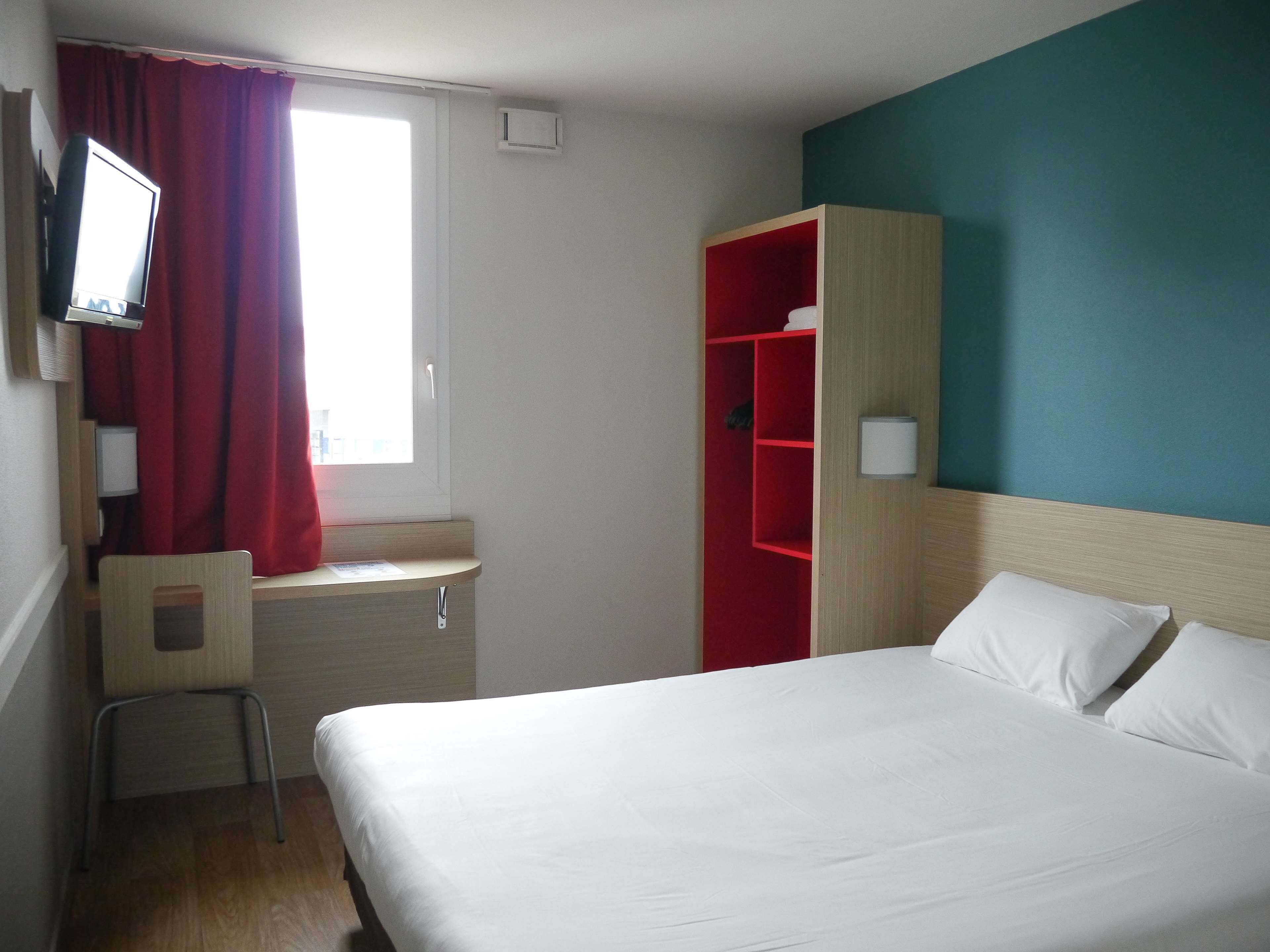 A hotel room with a bed, a desk, a chair, a TV, a wardrobe, and a window with curtains.