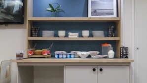 Een kitchenette met een blauwe wand, een lijst met een afbeelding en diverse etenswaren op planken.