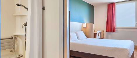 A hotel room with a bed, a shower, and a window with a red curtain.