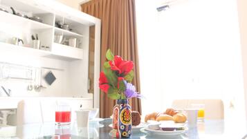 A breakfast table with a vase of flowers, croissants, and a glass of orange juice.