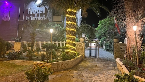 Entrada de un hotel de noche, con un camino de piedra, palmeras y una puerta enrejada.