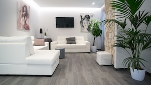 Un salón moderno con un sofá blanco, un sillón blanco más pequeño, un televisor de pantalla plana montado en la pared y una planta grande en maceta.