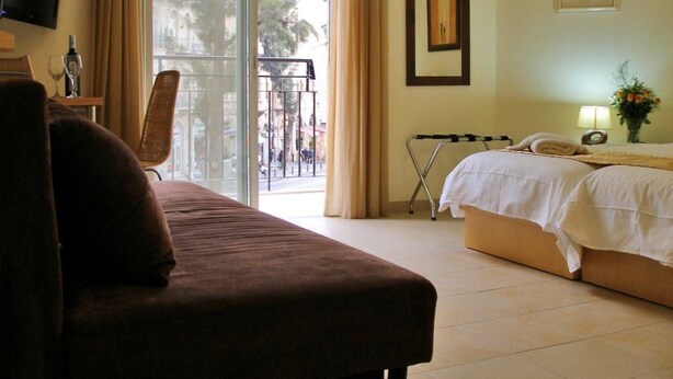 A hotel room with a sofa, a bed, a TV, a balcony with a view of the street, and a window with curtains. - City Center Jerusalem (Jerusalem)