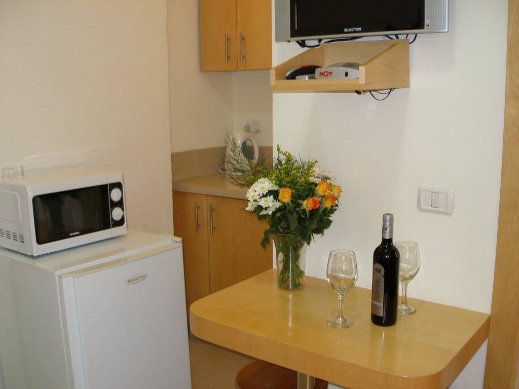 A compact kitchenette with a microwave, refrigerator, and a small table with a vase of flowers and wine glasses.