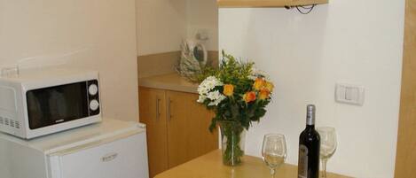 Una kitchenette compacta con microondas, refrigerador y una pequeña mesa con un florero y copas de vino.