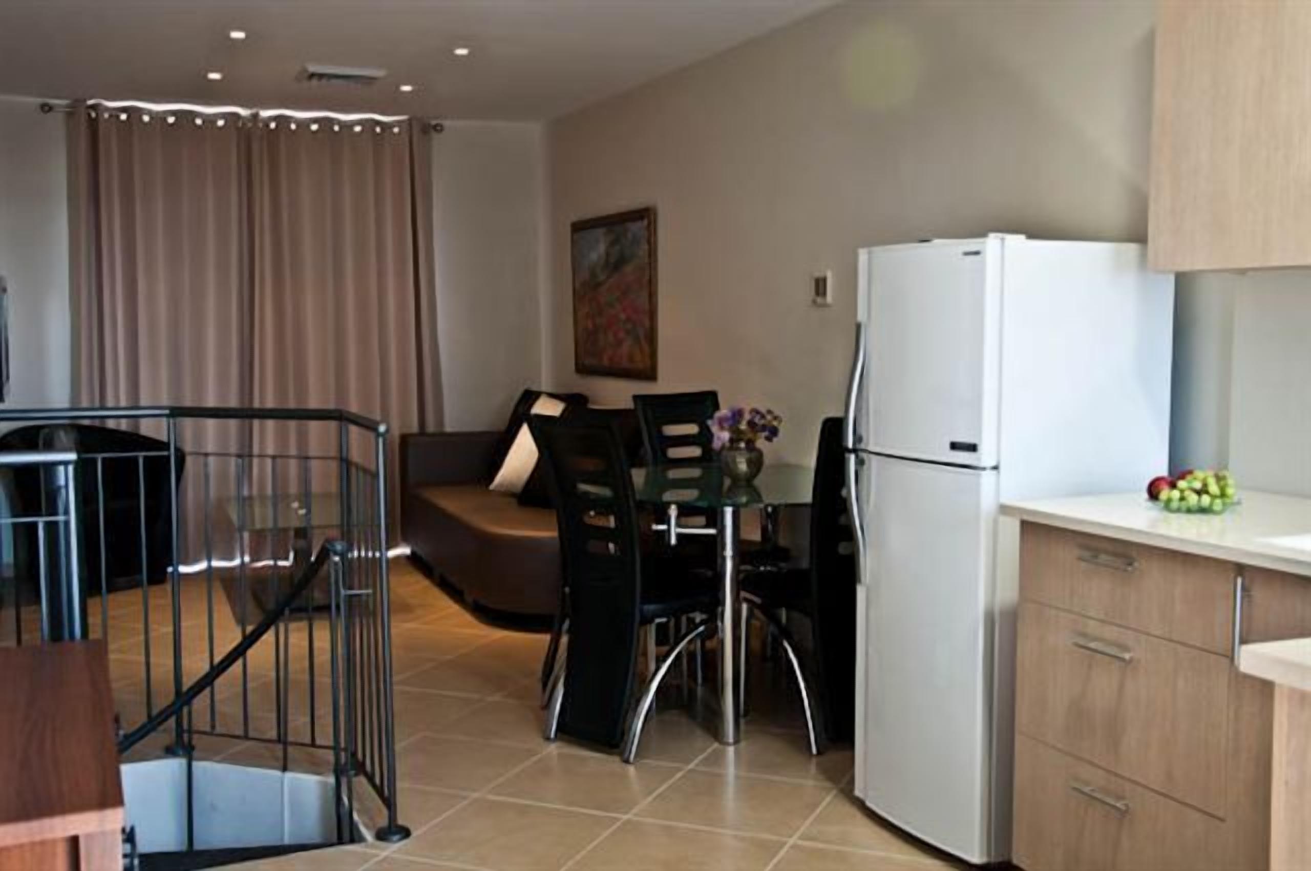 A modern kitchen with a white refrigerator, a dining table with chairs, and a staircase leading to a balcony.