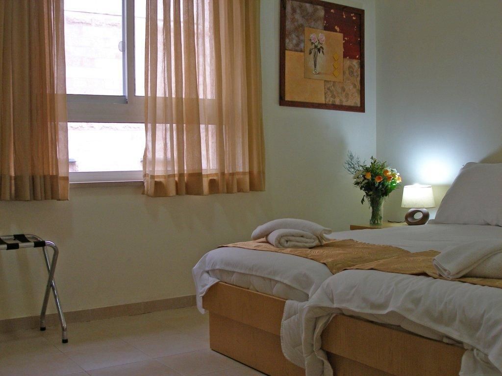 A hotel room with a bed, a bedside table with a lamp, a window with curtains, and a picture on the wall.