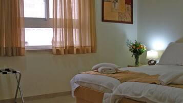 A hotel room with a bed, a bedside table with a lamp, a window with curtains, and a picture on the wall.