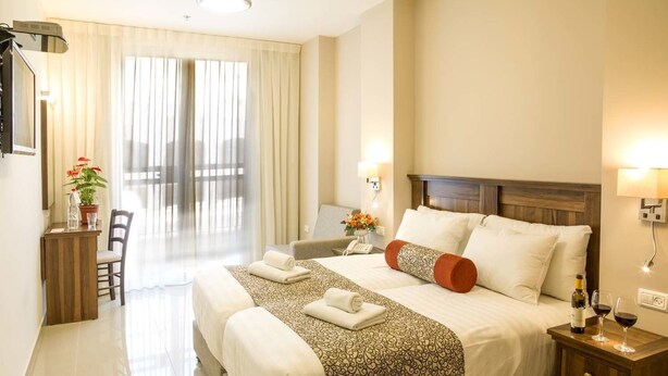 Ein Hotelzimmer mit einem großen Bett, einem Schreibtisch mit Stuhl, einem kleinen Tisch mit Flasche und Gläsern sowie Blick durch das Fenster nach draußen.