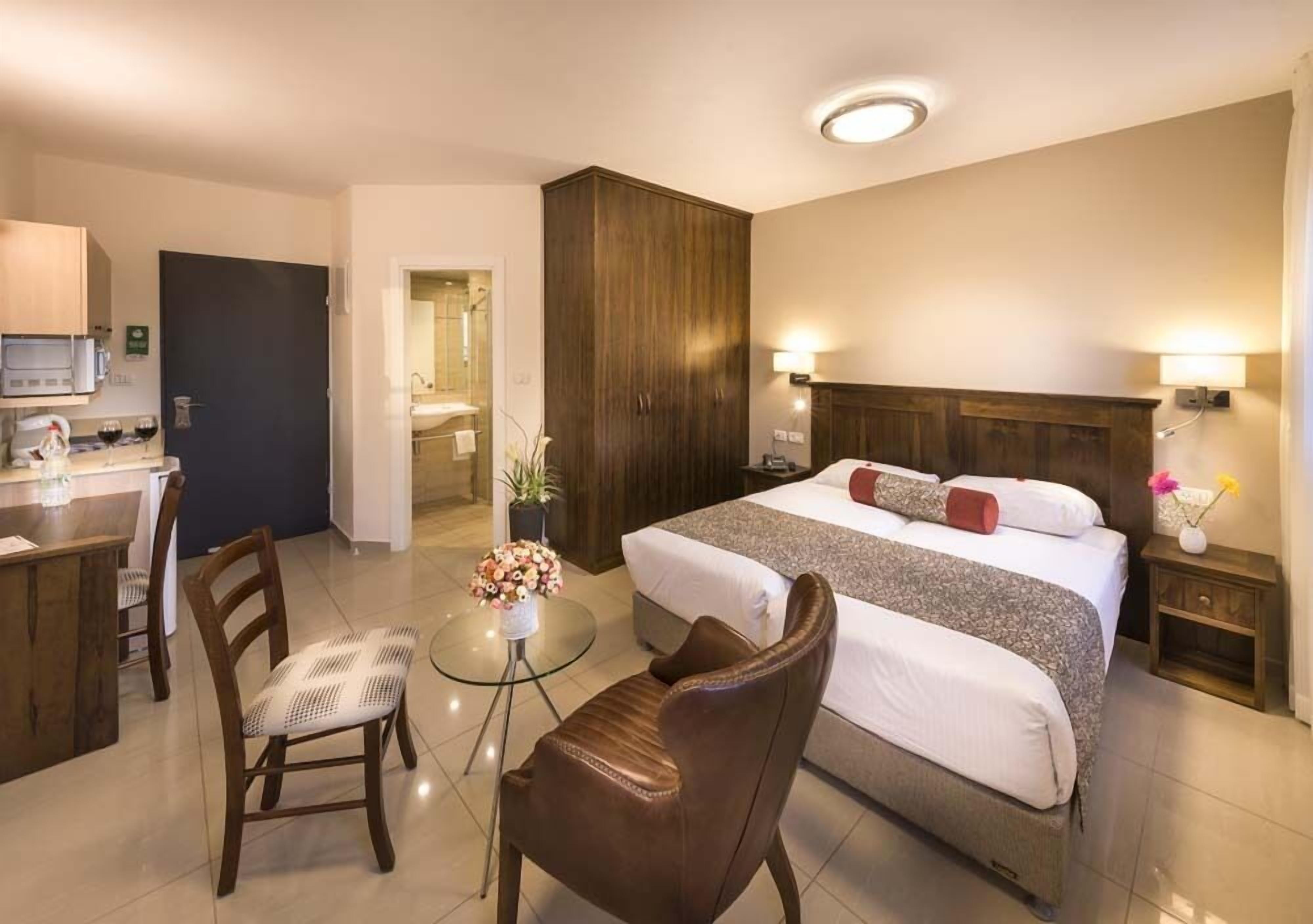 A hotel room with a bed, a desk, a chair, and a small table with a vase of flowers.
