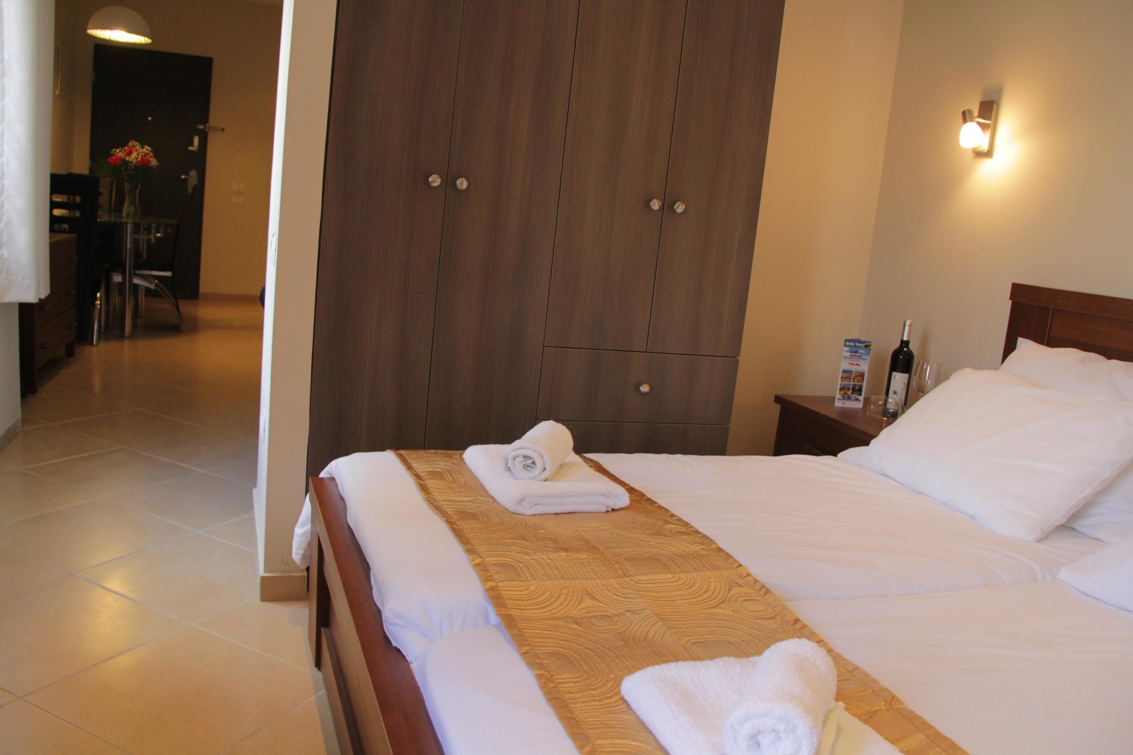 A hotel room with a bed, wooden wardrobe, nightstand, and a bottle of wine.