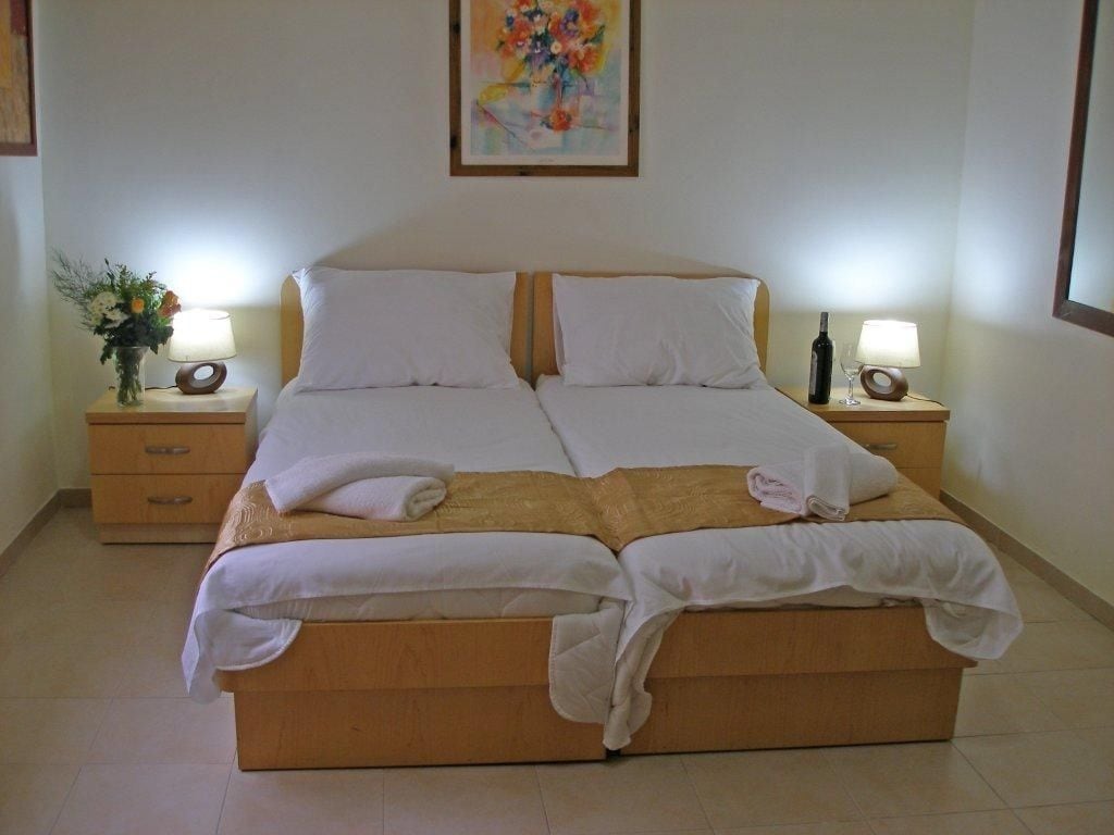 A double bed with white linens, two bedside tables with lamps, and a floral painting on the wall.