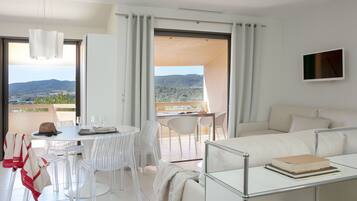 Una habitación moderna y luminosa con un balcón, un área de comedor con sillas y una mesa, y un sofá con un libro encima.