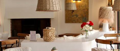 Una sala de estar acogedora con chimenea, lámparas de mimbre y muebles blancos.