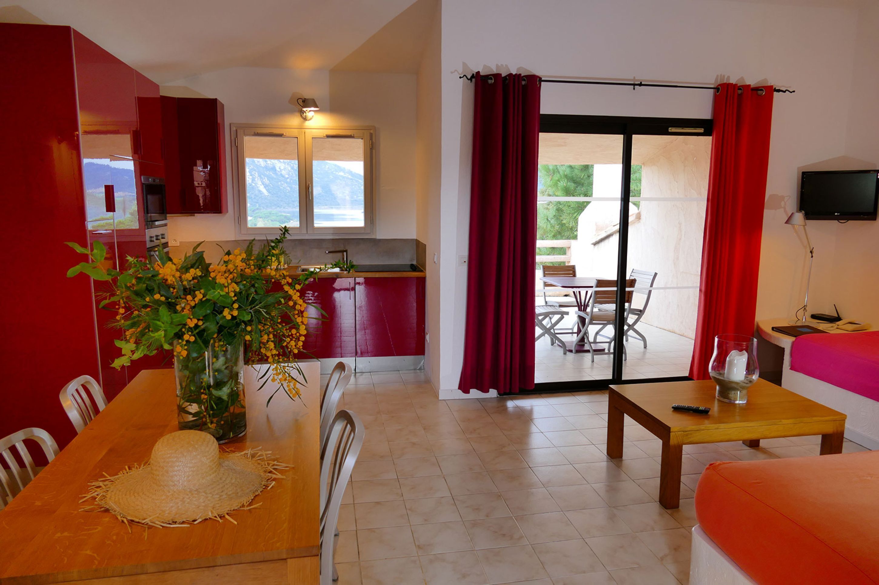 A room with a dining table, chairs, a kitchen area, a sofa, and a TV.