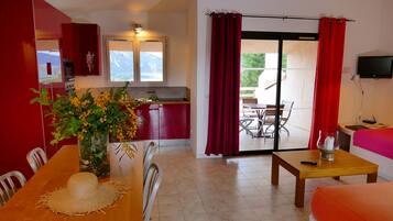 A room with a dining table, chairs, a kitchen area, a sofa, and a TV.