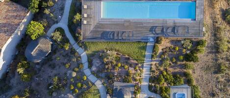 Vista aérea de un resort con una amplia piscina rectangular, un jacuzzi independiente y un camino sinuoso.
