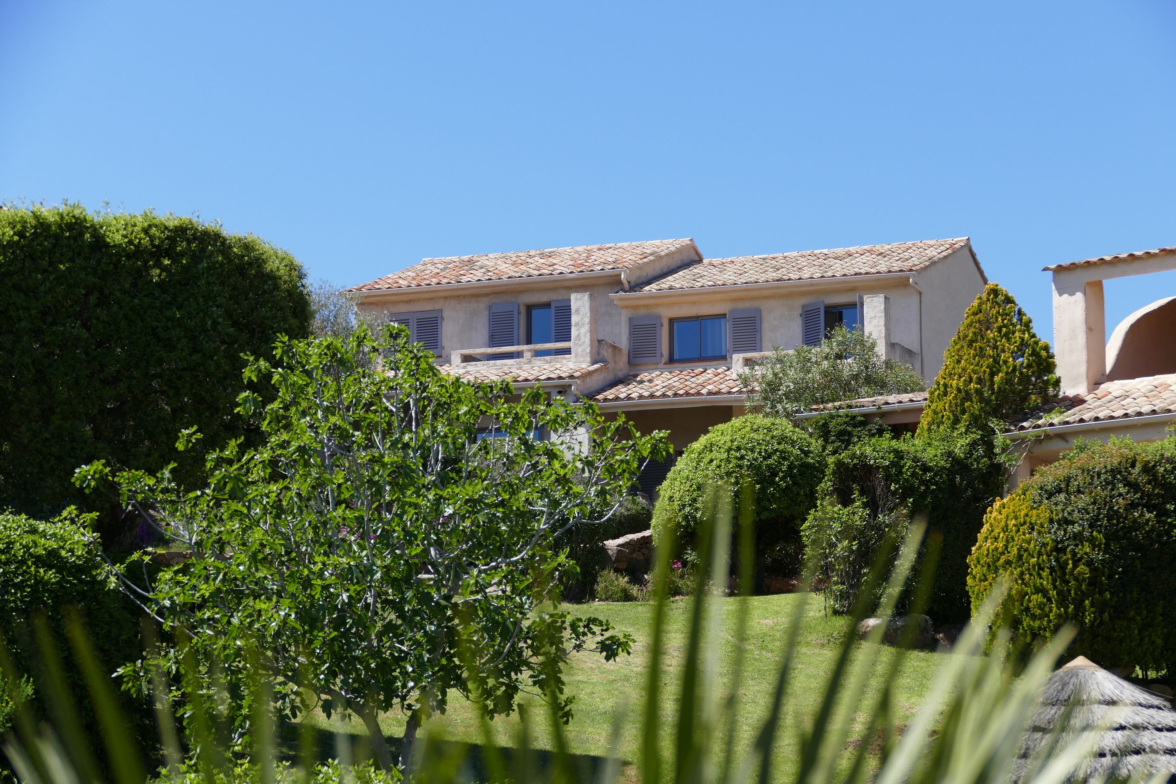 A two-story house with a tiled roof, surrounded by well-maintained gardens and trees.