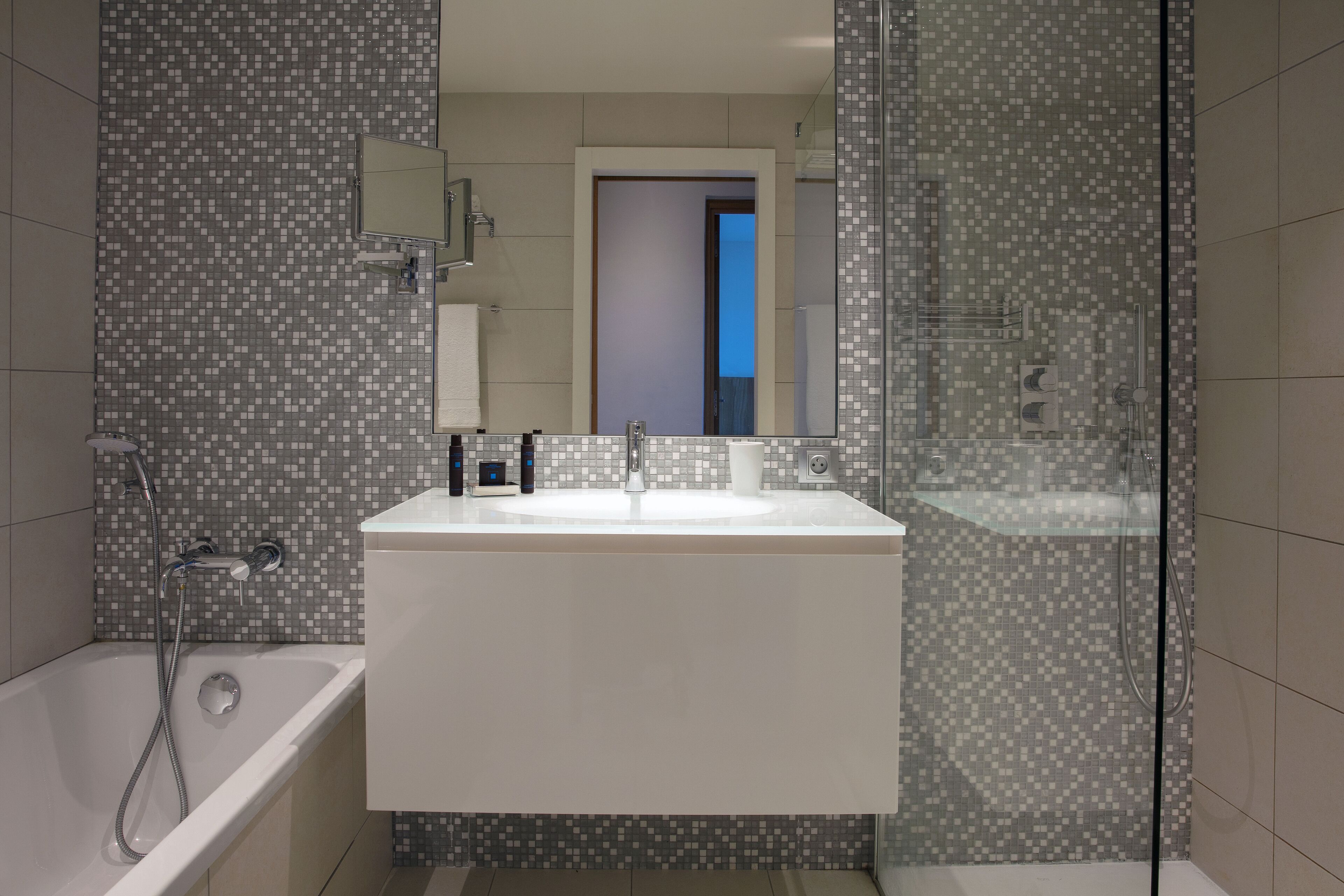 Ein modernes Badezimmer mit einem weißen Waschbecken, einer Duschkabine aus Glas und einem Fliesenboden.