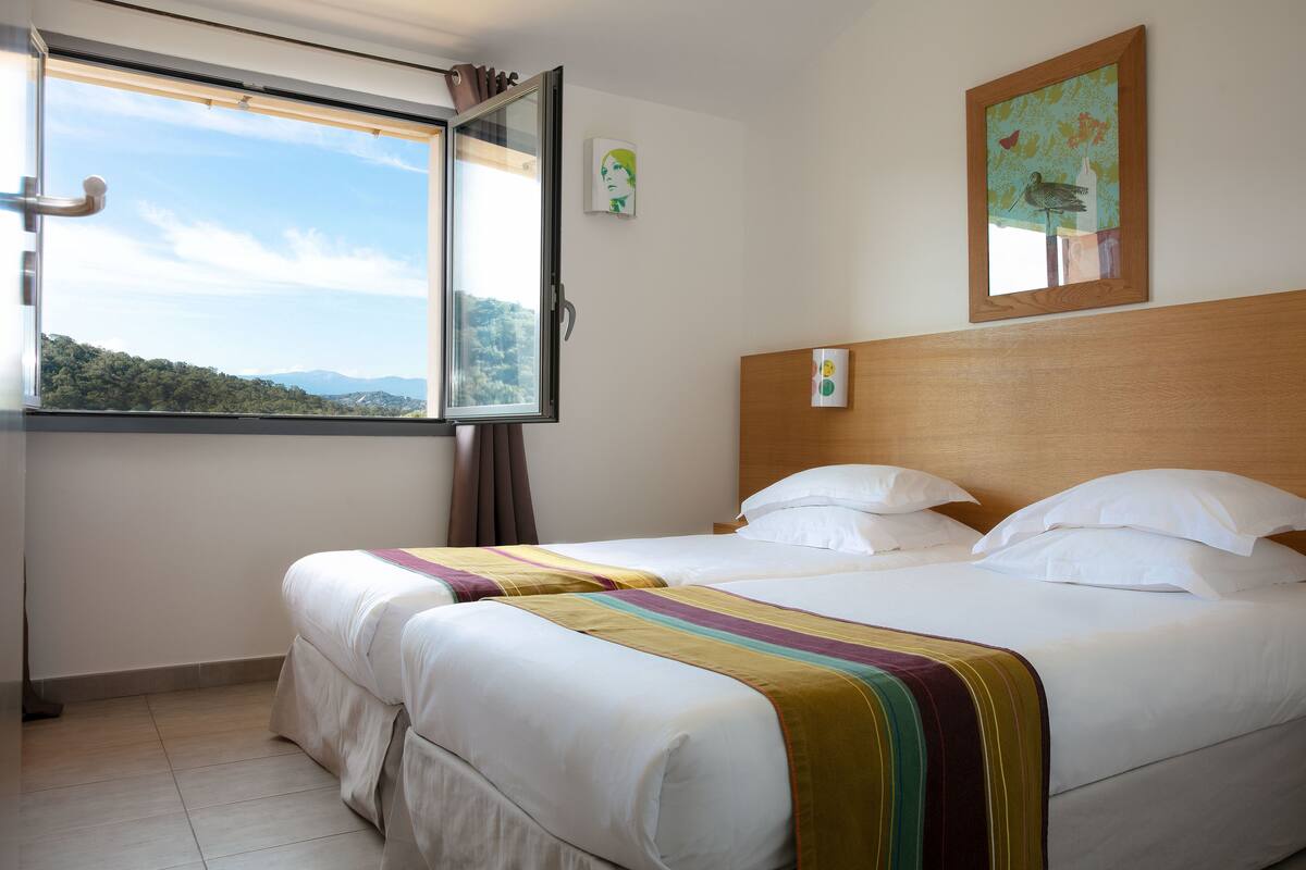 Une chambre d’hôtel avec deux lits, une fenêtre donnant sur les montagnes et une tête de lit en bois.