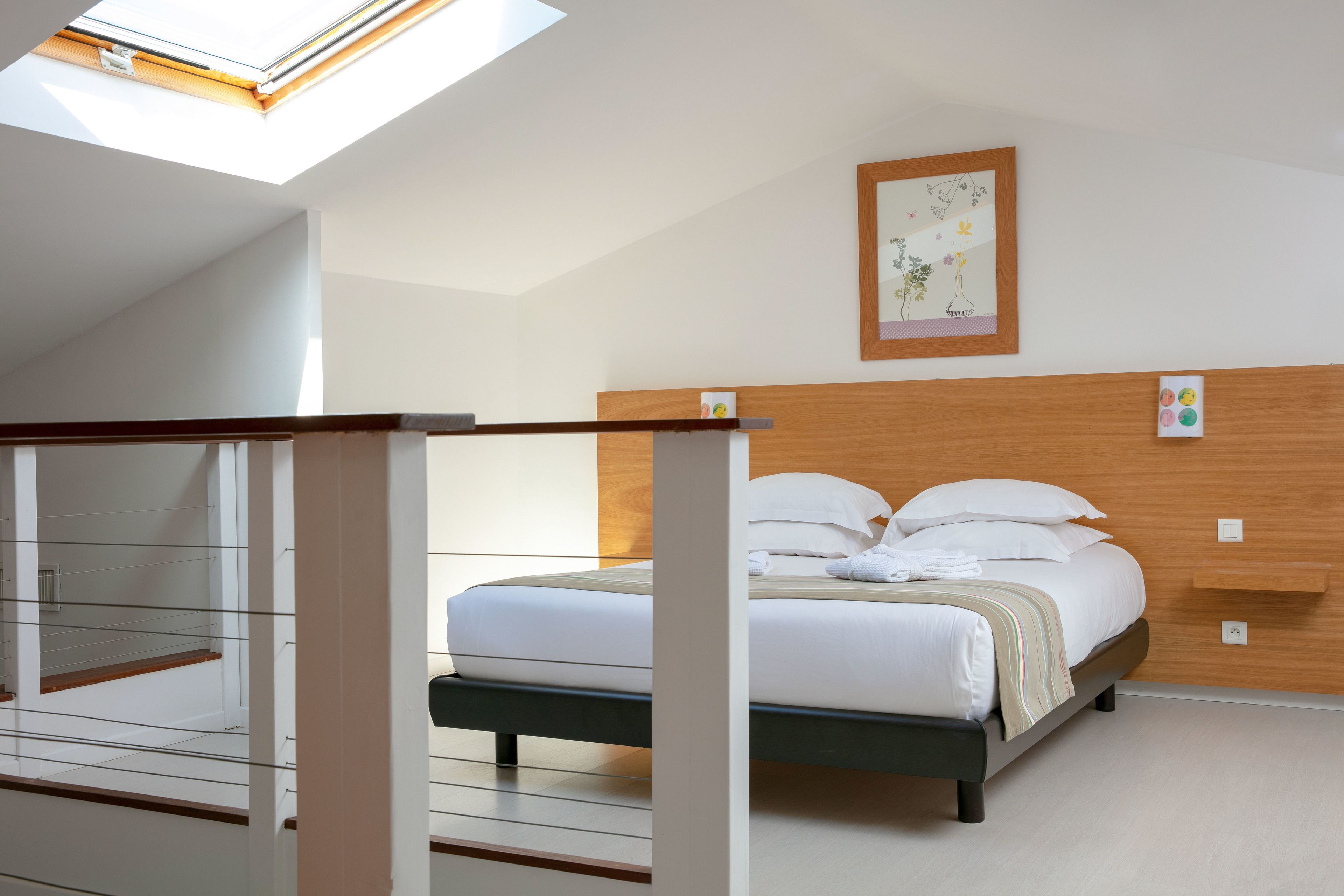 Une chambre à coucher avec un lit, une lucarne, une tête de lit en bois et une étagère fixée au mur.