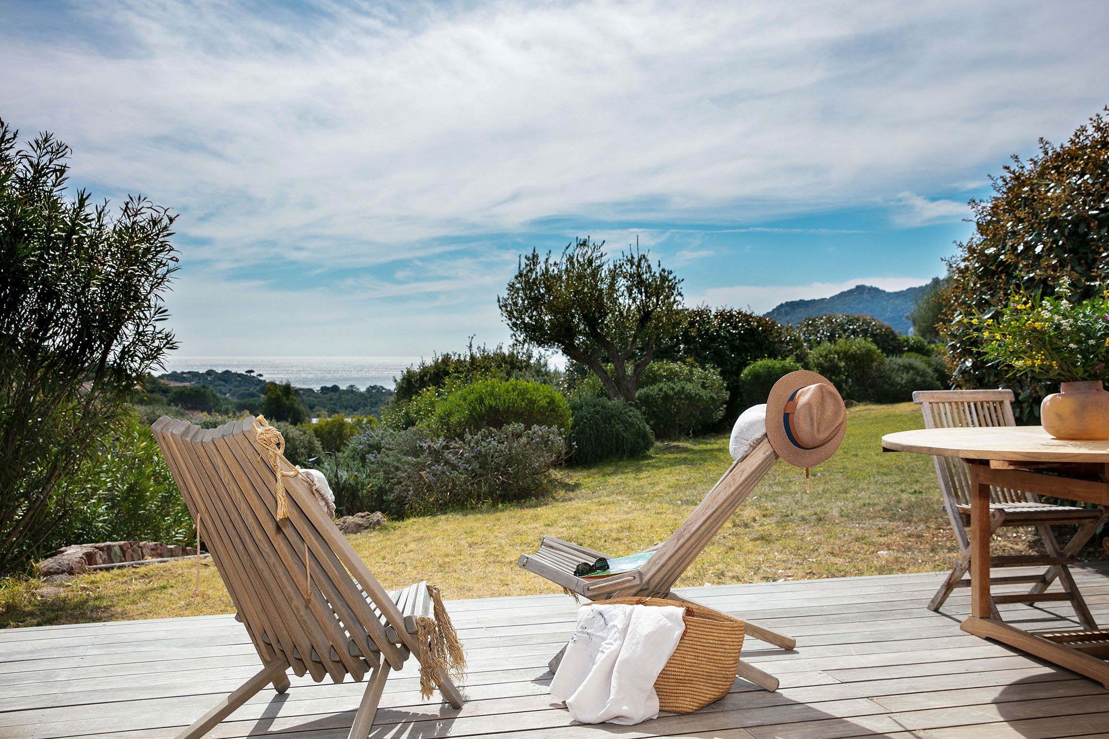 Eine Holzterrasse mit zwei Liegestühlen, einem Tisch und einem Hut.