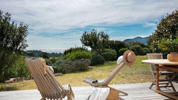 Eine Holzterrasse mit zwei Liegestühlen, einem Tisch und einem Hut.
