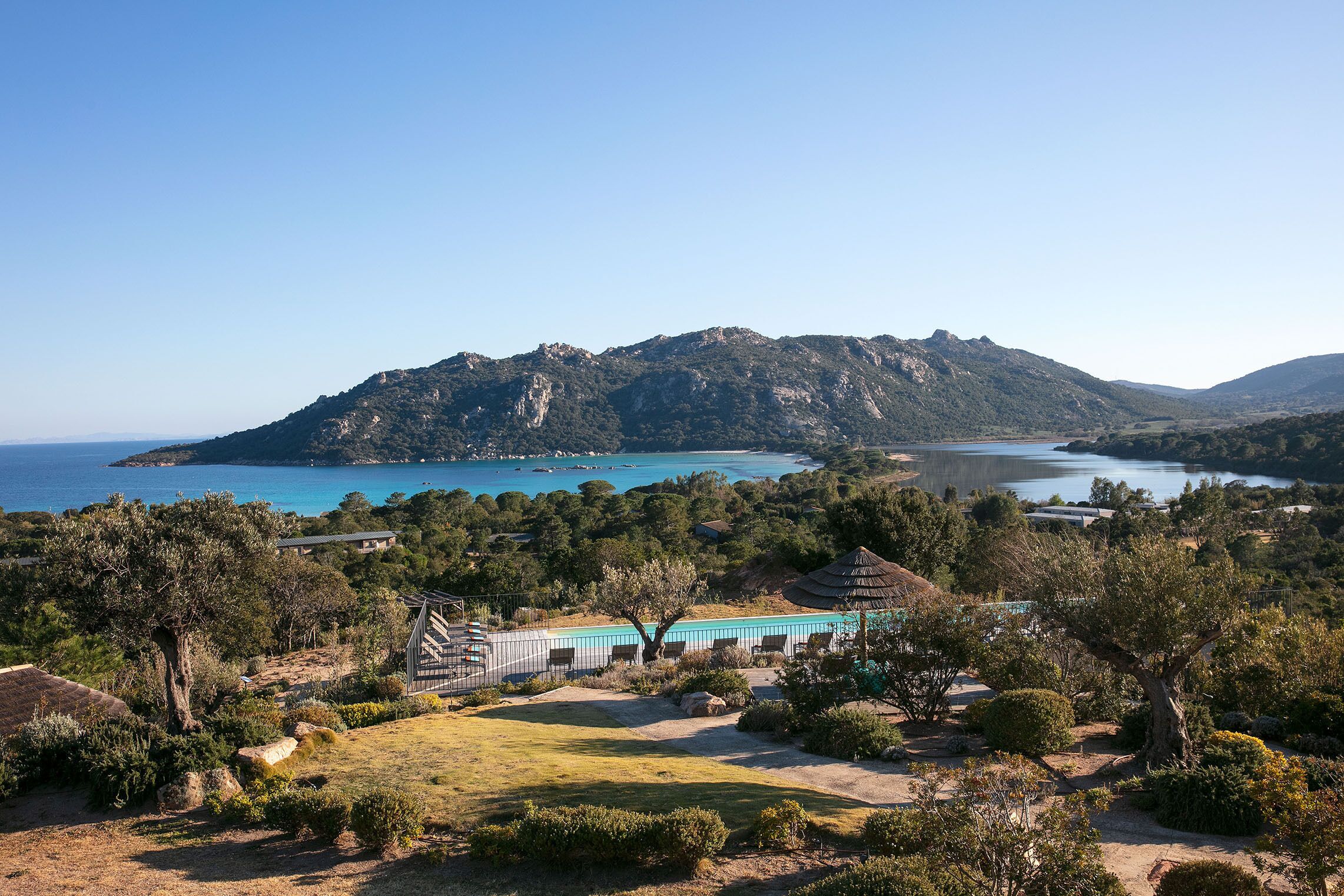 A coastal landscape with a mountain, a body of water, and a building with a blue roof.