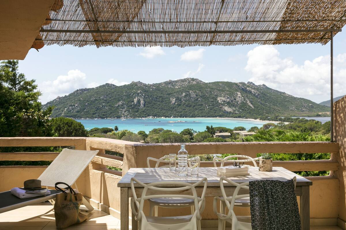 Une terrasse avec une table et des chaises donnant sur un paysage montagneux et un plan d’eau.