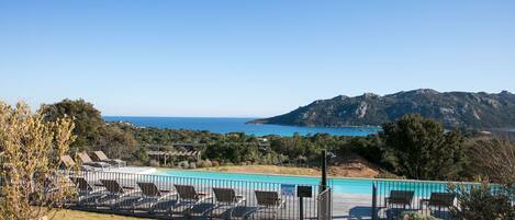 A pool area with lounge chairs and a view of the sea and mountains.