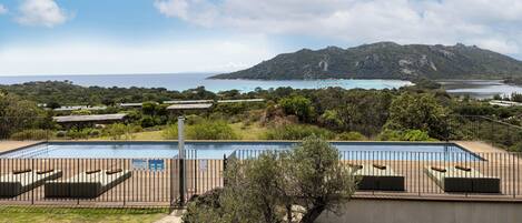 A pool area with a view of the sea and a mountain in the background.