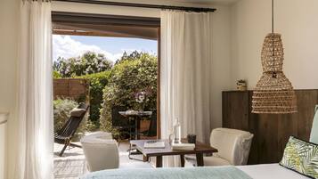 A bedroom with a bed, a desk, and a chair. There is a view of a garden outside.