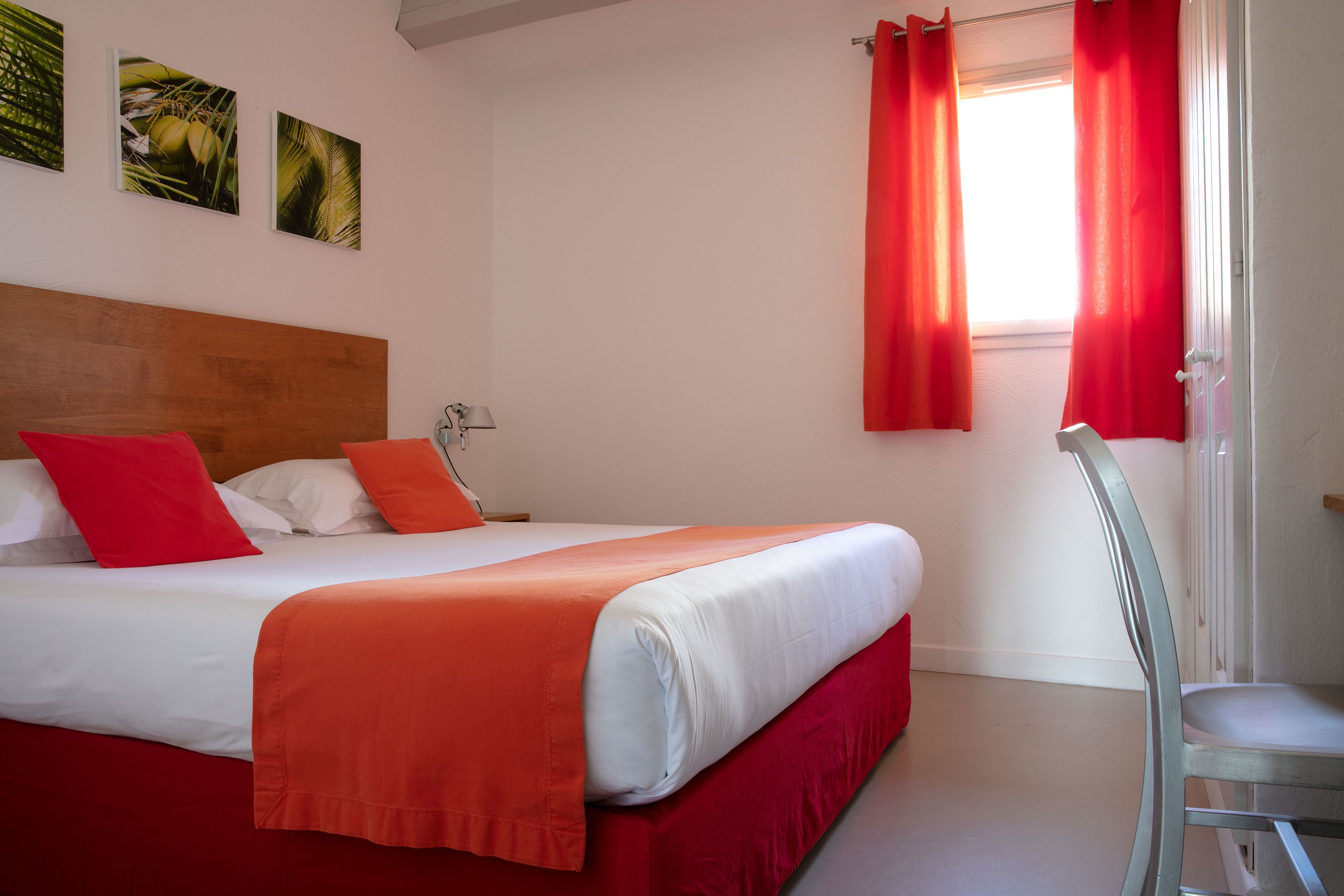 Une chambre d’hôtel avec un lit, des rideaux rouges et une chaise.