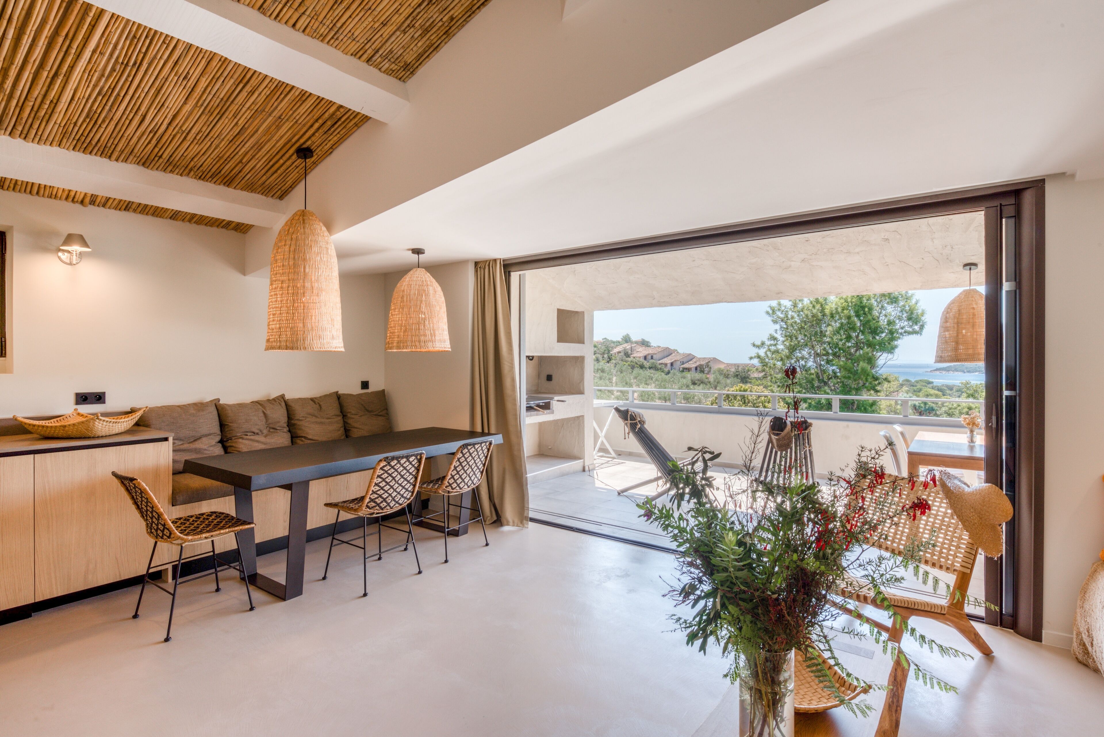 A modern kitchen with a dining area, large windows, and a balcony with a view.