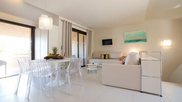 A modern living room with a dining area, white furniture, a flat-screen TV, and a painting on the wall.