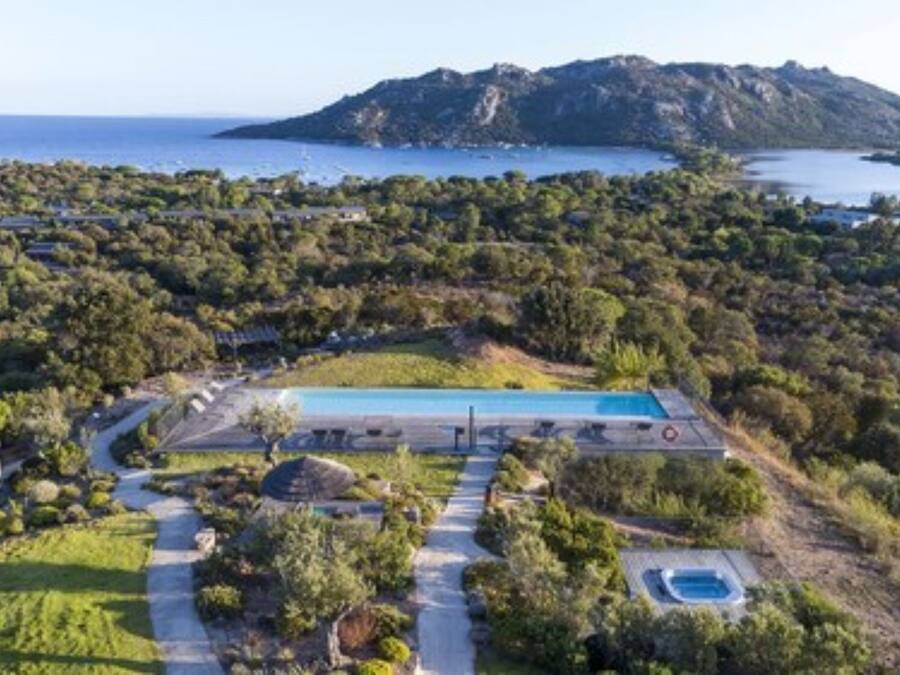 Vue aérienne d’une propriété dotée d’une piscine, d’un grand bâtiment et ayant une chaîne de montagnes en arrière-plan.