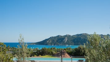A coastal view with a clear sky, a swimming pool, and a mountainous backdrop.