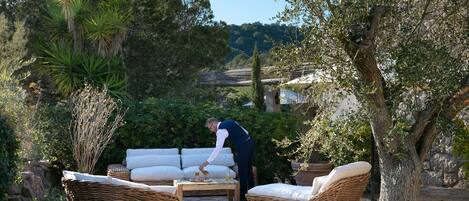 Un espace patio aménagé avec des meubles en osier, une table en pierre et une personne qui s’occupe d’une plante.