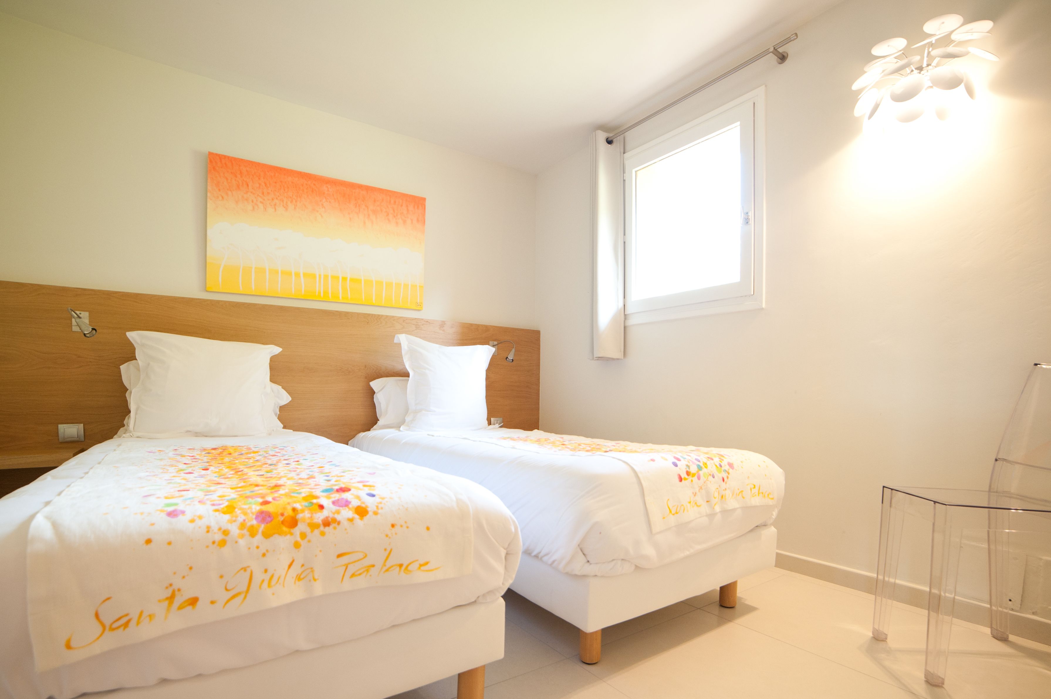 A hotel room with two beds, a wooden headboard, a painting on the wall, a window, and a clear chair.