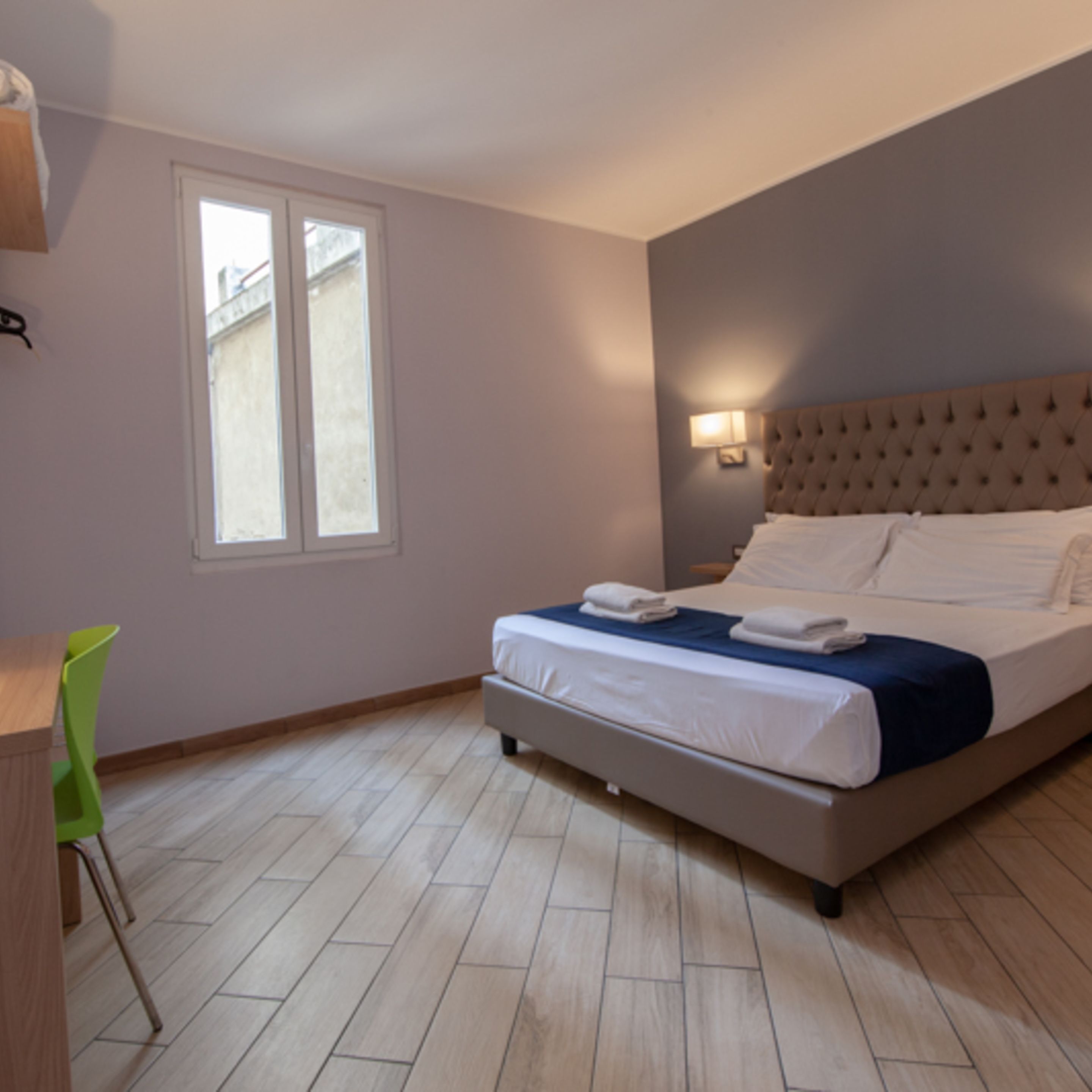 Un dormitorio con cama, ventana, silla y escritorio.