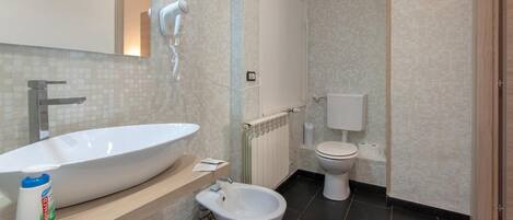 A modern bathroom with a large white sink, a bidet, a toilet, and a hairdryer mounted on the wall.