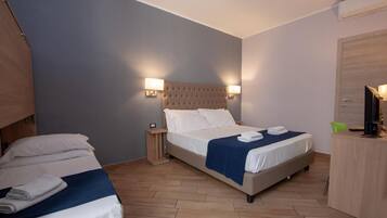 Ein Hotelzimmer mit zwei Betten, Holzboden, einem Kopfteil mit Wandleuchten, einem Schreibtisch mit Stuhl und einer Tür.