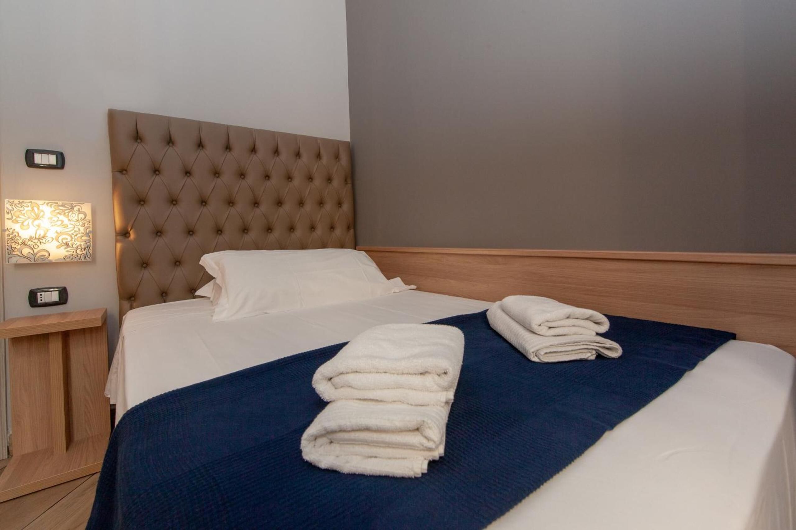 A neatly made bed with a tufted headboard, a blue blanket, and folded towels.
