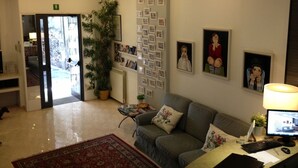 Un espace d’accueil comprenant un canapé, un bureau avec un ordinateur, une lampe et une plante en pot.