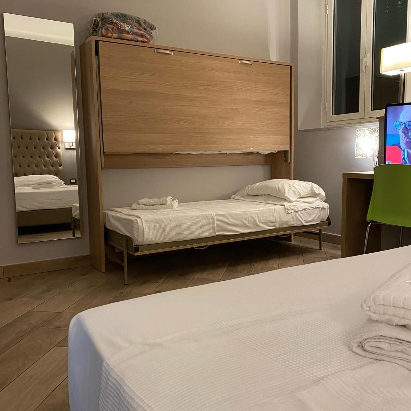 Une chambre avec un lit simple, une tête de lit en bois, un miroir et un téléviseur.