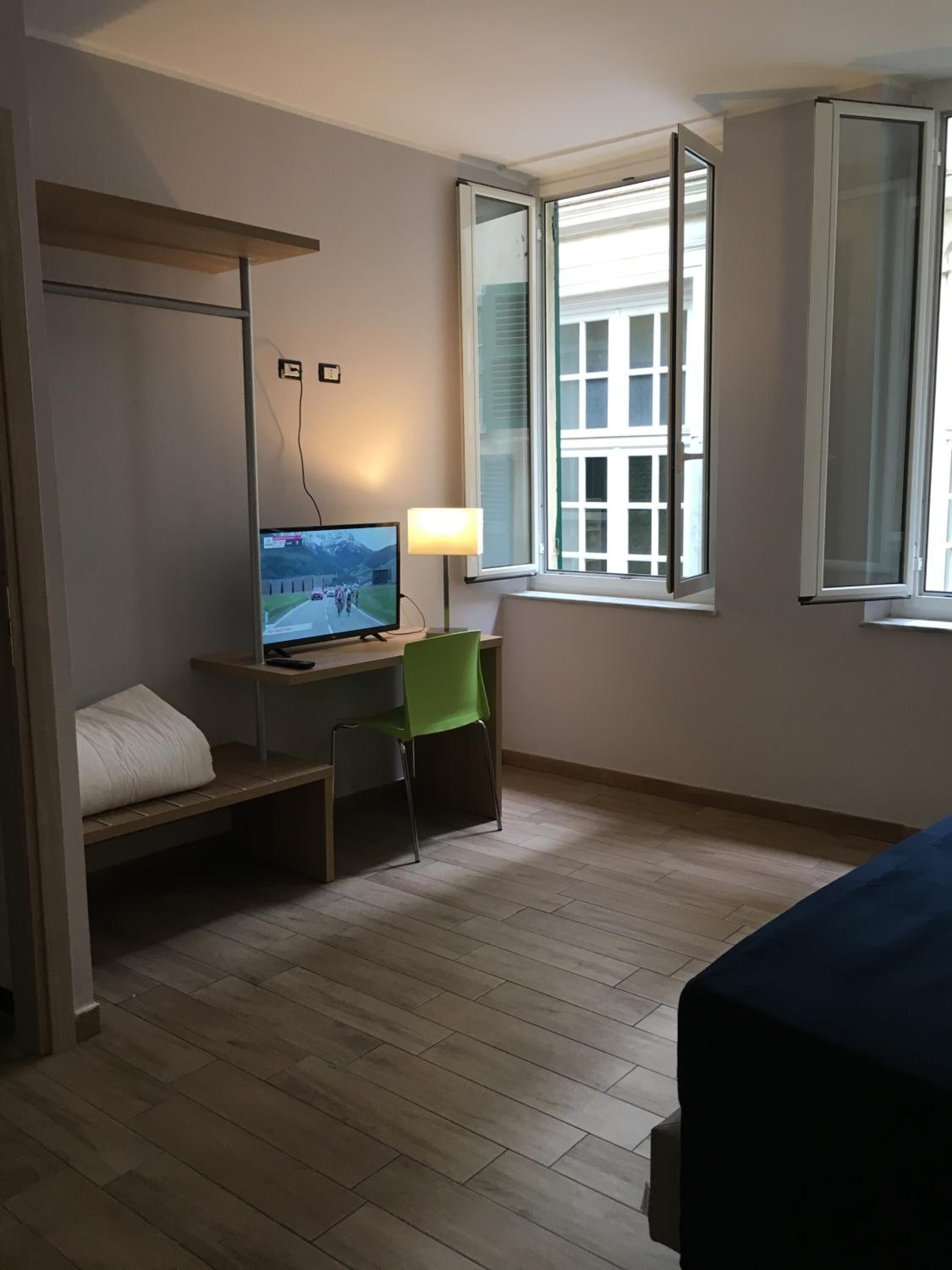 Ein Hotelzimmer mit Etagenbett, einem Schreibtisch mit Computer, einem Stuhl und einem Fenster mit Blick auf Gebäude.