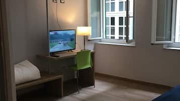 Ein Hotelzimmer mit Etagenbett, einem Schreibtisch mit Computer, einem Stuhl und einem Fenster mit Blick auf Gebäude.