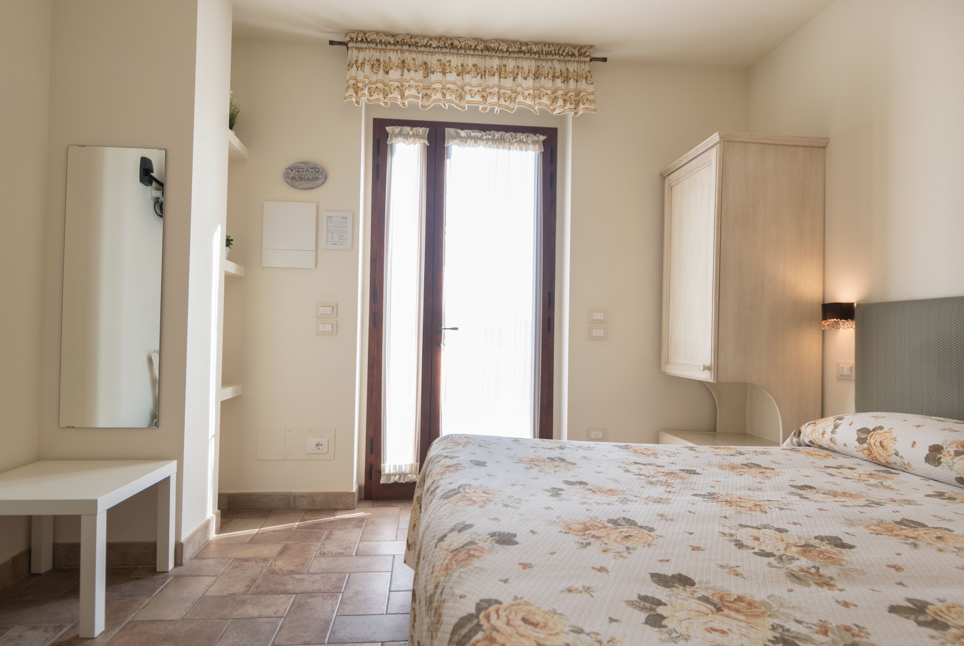 A bedroom with a bed, a bedside table, a wardrobe, a mirror, and a window with curtains.