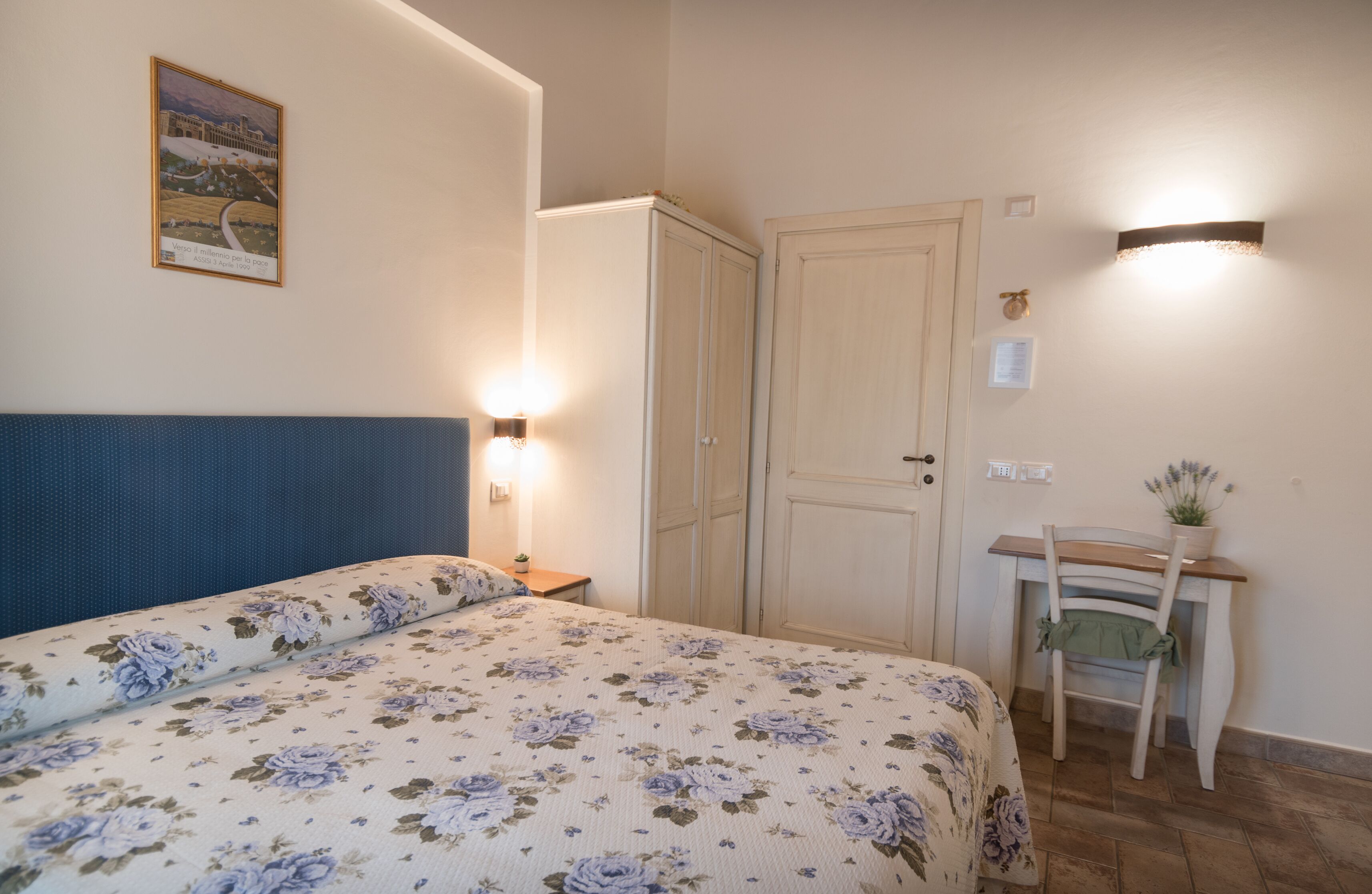 Un dormitorio con cama, armario, escritorio con silla y lámpara de pared.